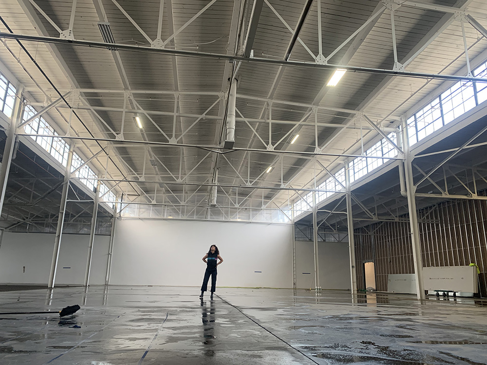 woman stands in an empty part of a cleared out warehouse