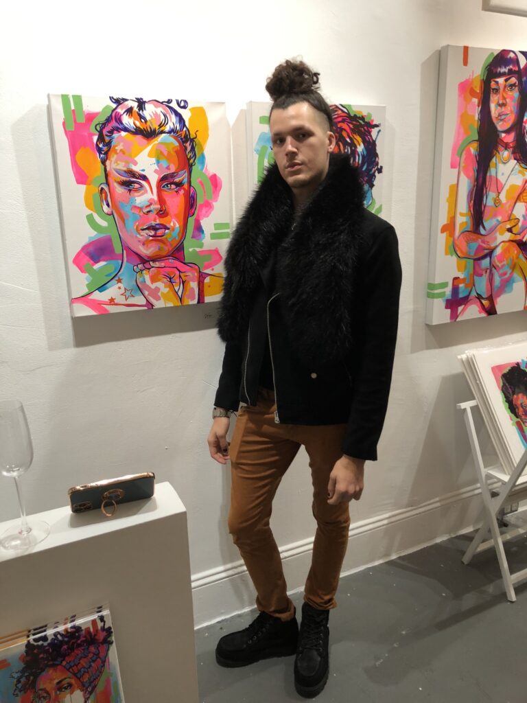 man in man bun stands in front of brightly colored portrait of himself