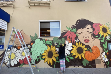 woman stands in front of a mural painting it