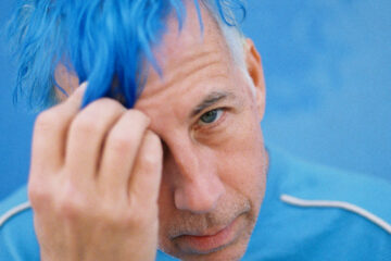Man tugs blue hair and looks at camera