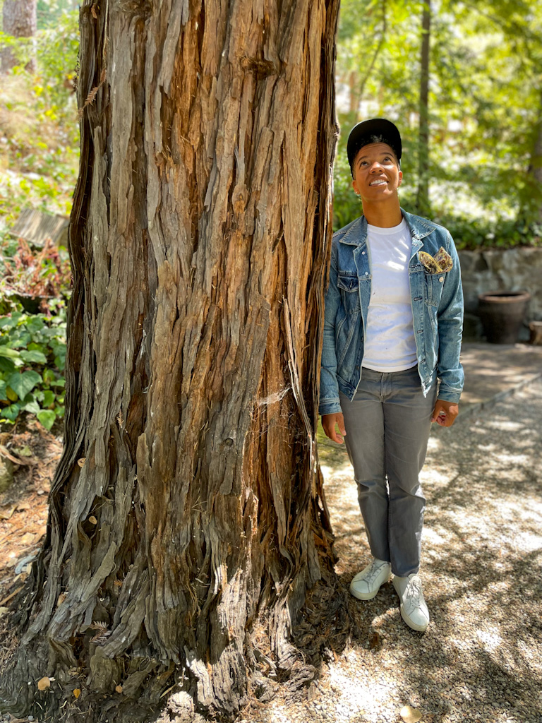 Nenna Joiner stands beside a towering redwood tree.