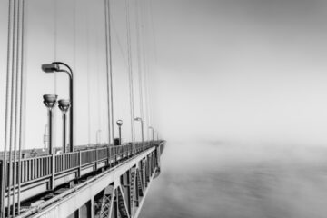 The deck of the Golden Gate Bridge seemingly disappearing into fog. Photo rendered in black-and-white.