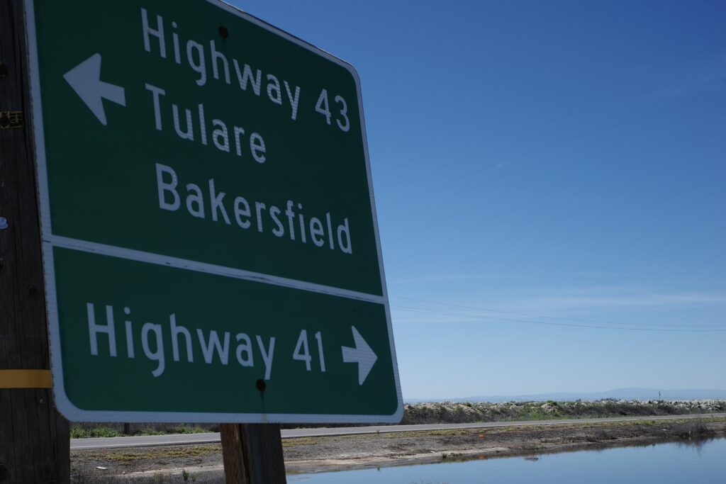 A green sign pointing left for Highway 43, Tulare & Bakersfield, and pointing right for Highway 41 with flood waters below.
