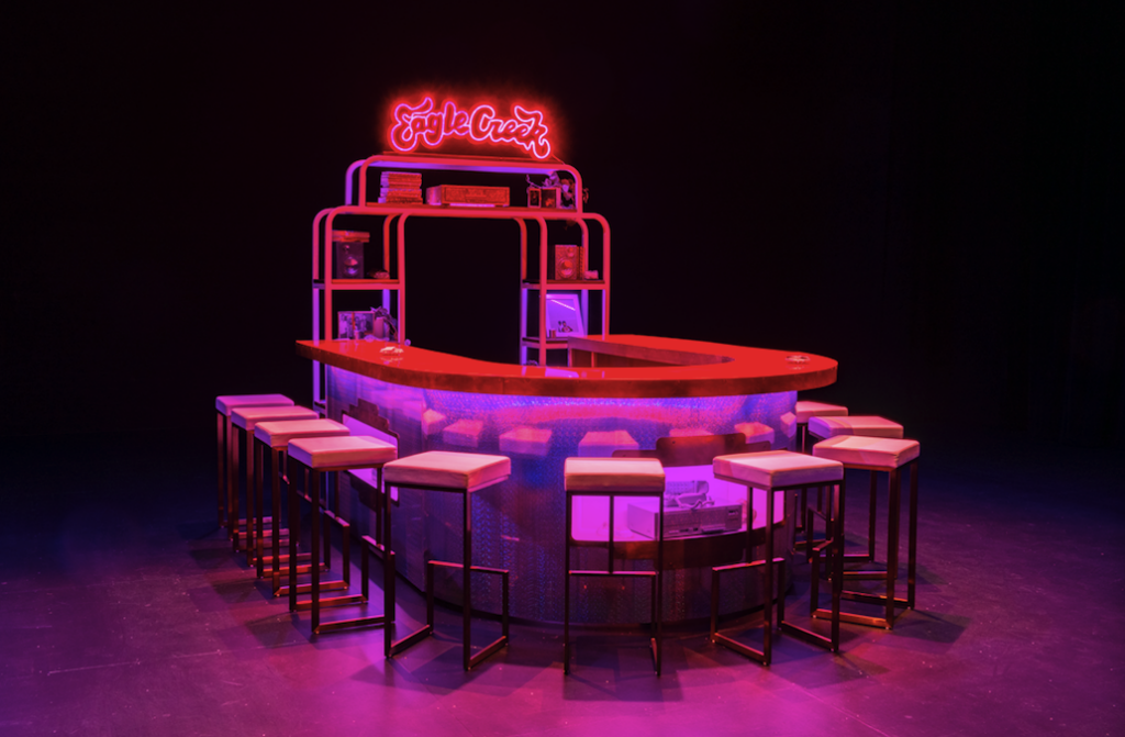 Description: A neon backlit retro stand alone bar surrounded by barstools with "Eagle Creek" in neon hanging above the back shelving.